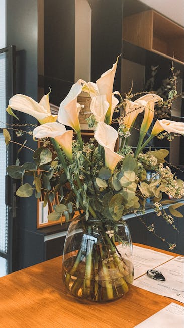 A bouquet arrangement of large, elegant cream-colored calla lilies with smooth, curved petals, complemented by sprigs of small white filler flowers and rounded green eucalyptus leaves, all beautifully